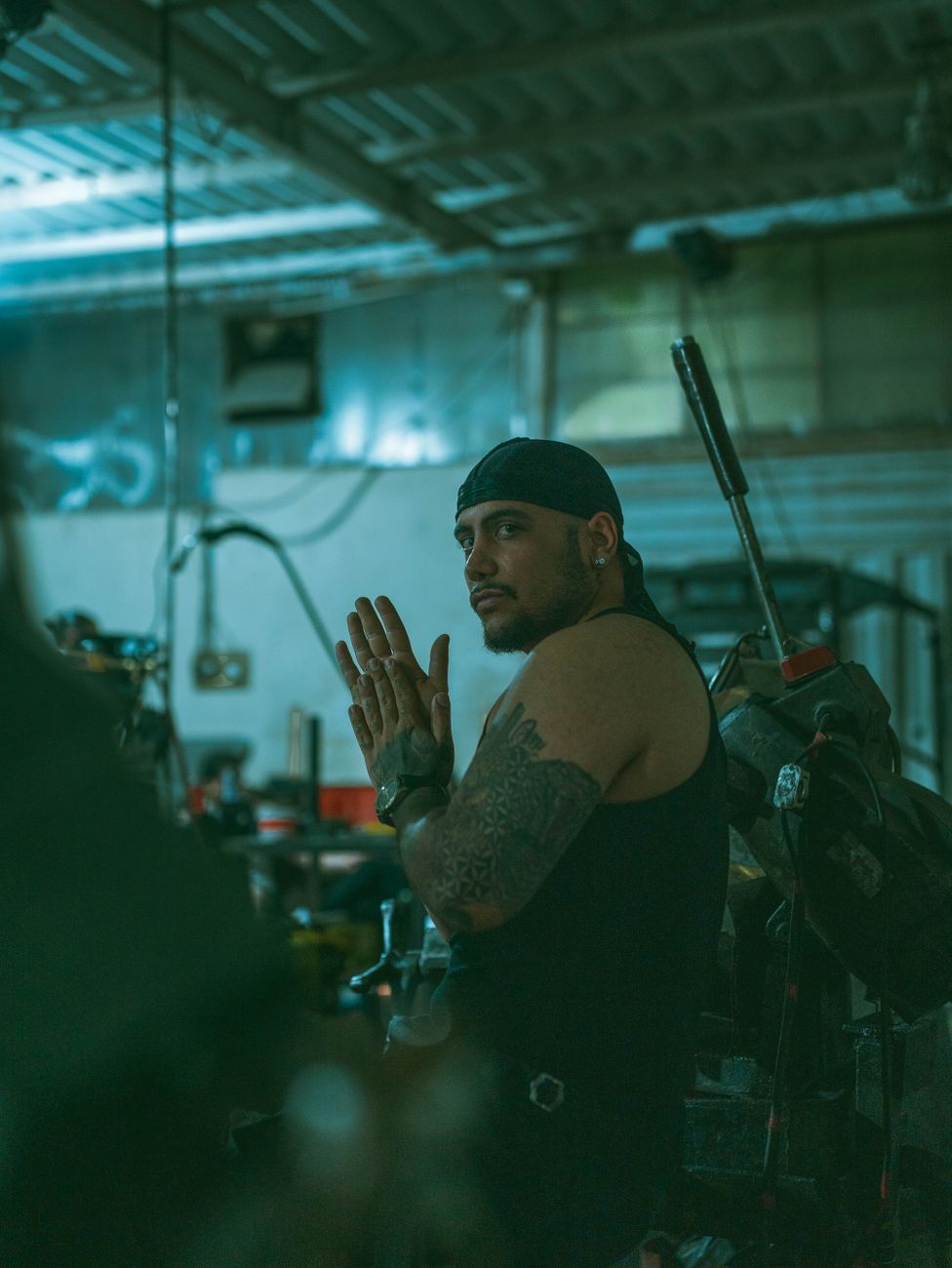 A rugged tattooed mechanic in a dimly lit workshop, deep in thought.