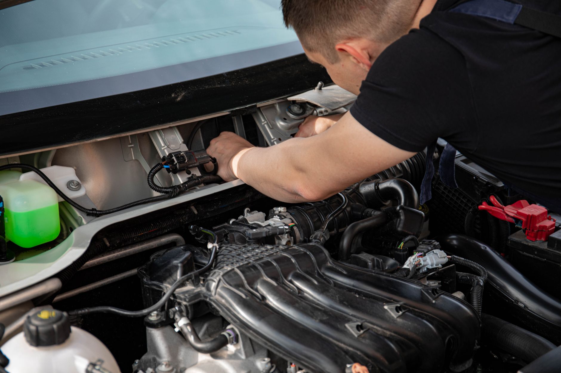 Photo of a mechanic working under a car hood on the engine