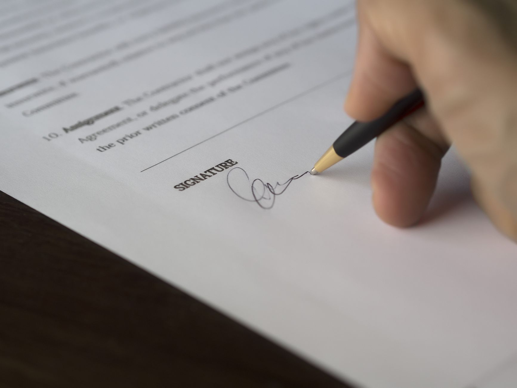 A hand signing a document with a pen on a wooden desk