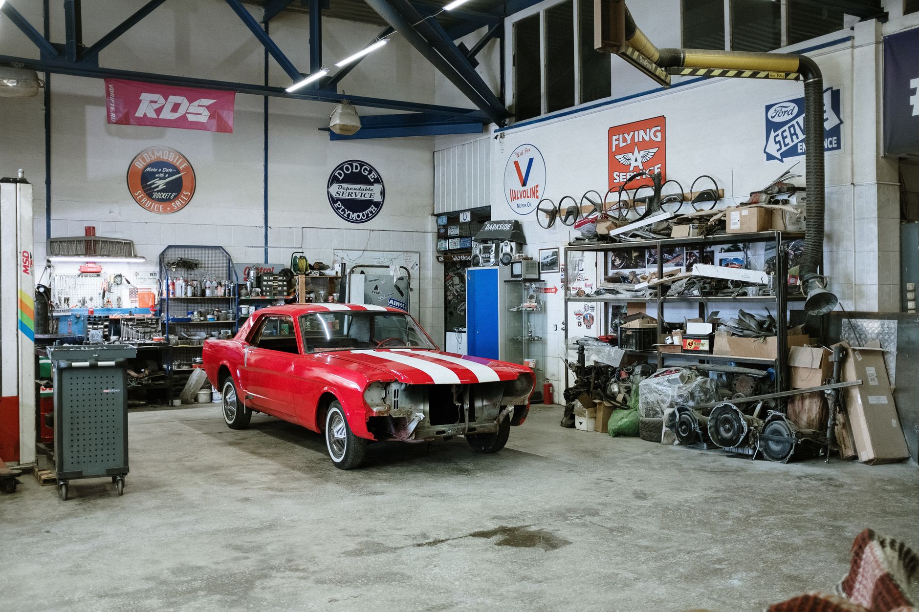 A vintage red car being restored in a workshop full of tools and parts