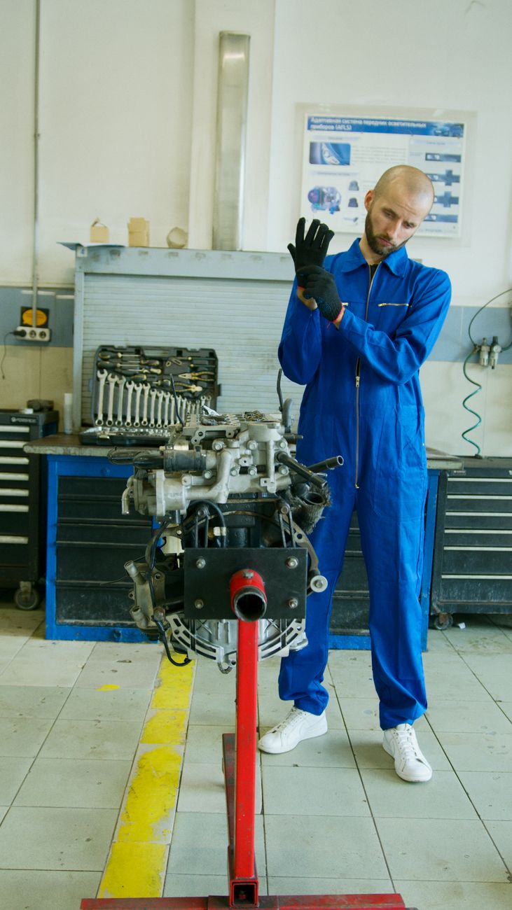 A mechanic in blue overalls adjusting his gloves beside an engine