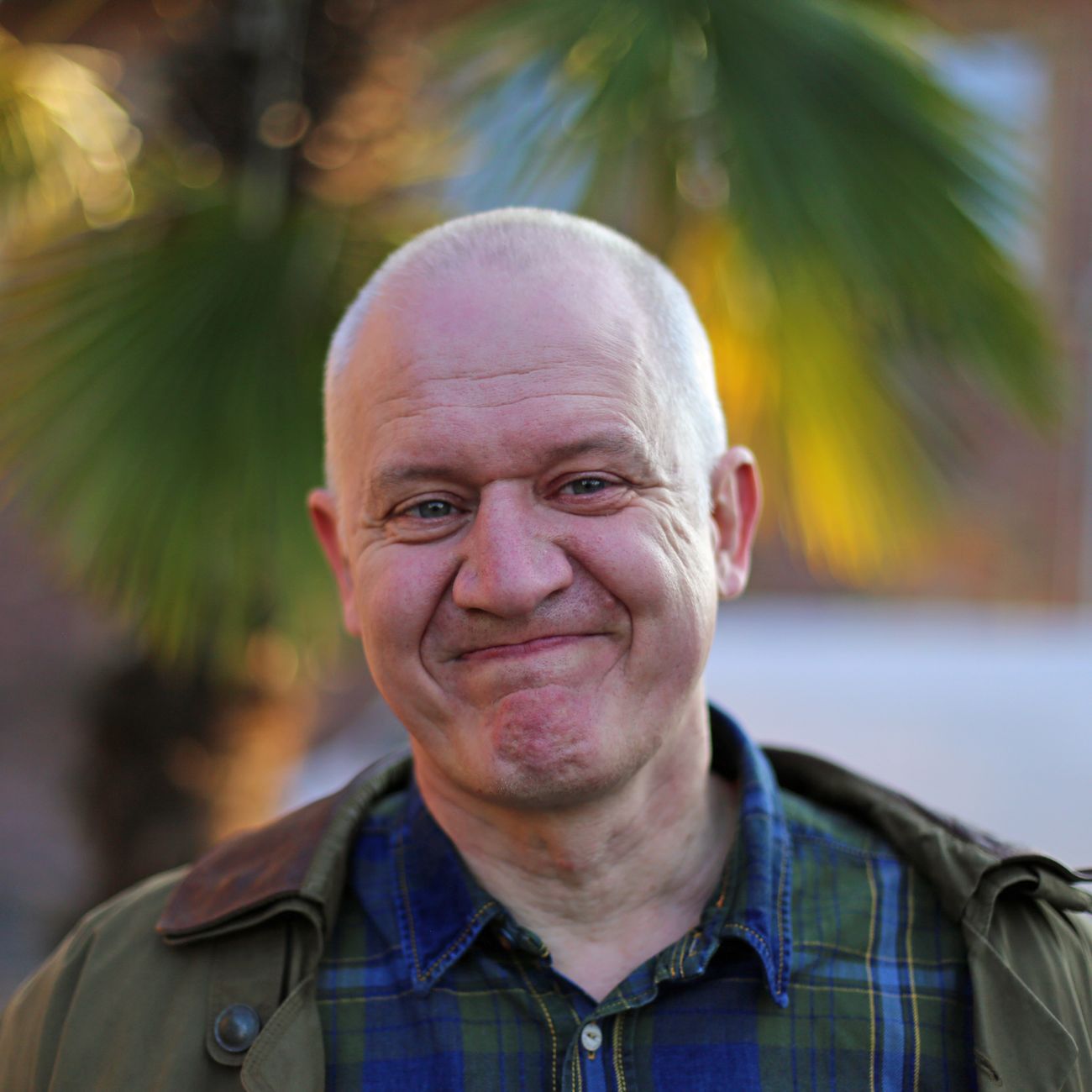 A smiling bald man outdoors in front of palm trees