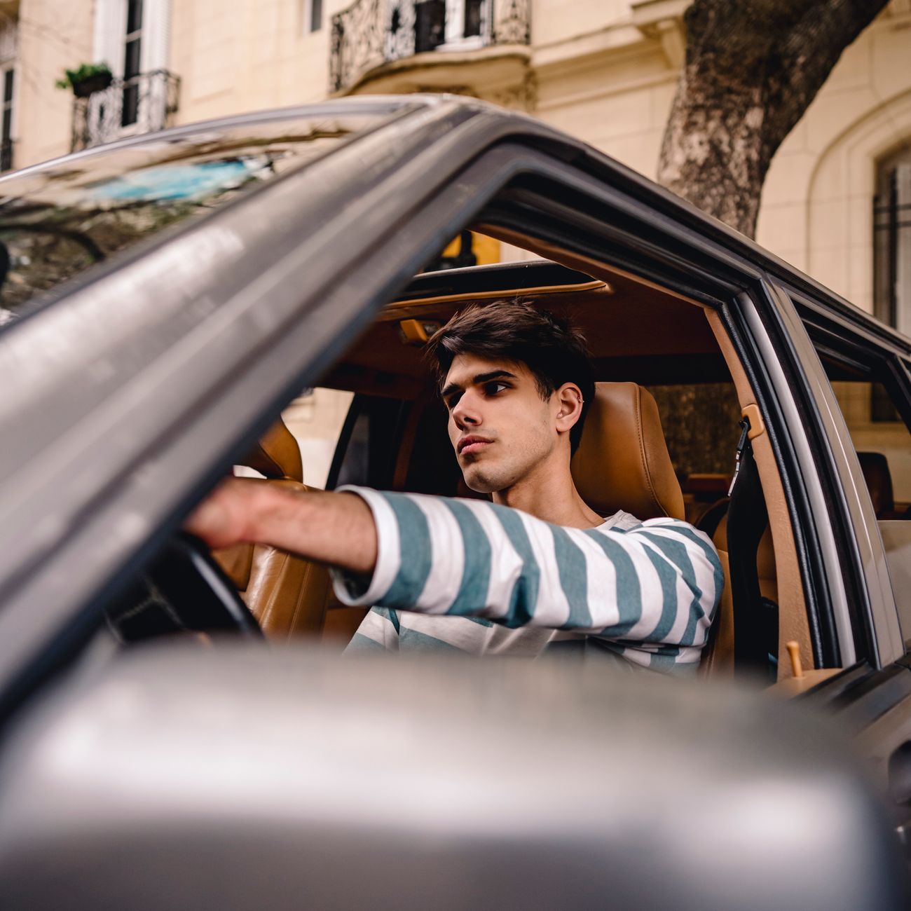 A smiling young man behind the wheel of a car on a city street