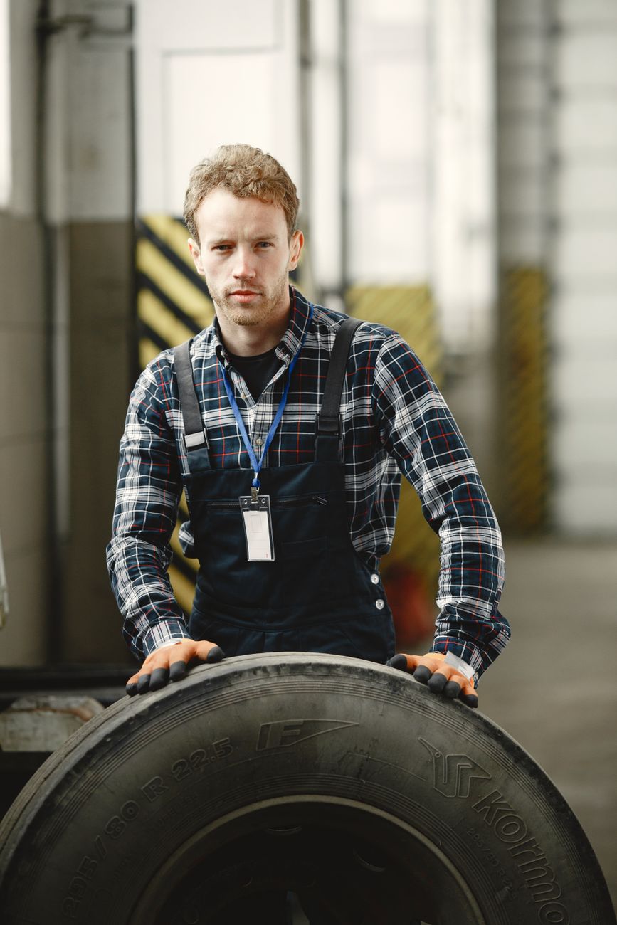 A mechanic holding a large tyre in a garage workshop