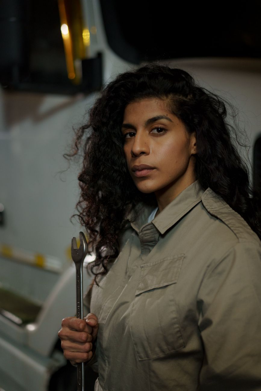 A woman auto mechanic holding a wrench in front of a truck