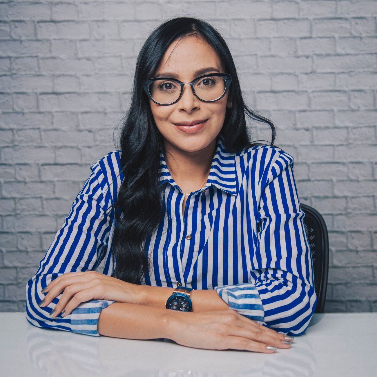 A young woman in a striped shirt and glasses sitting with arms crossed