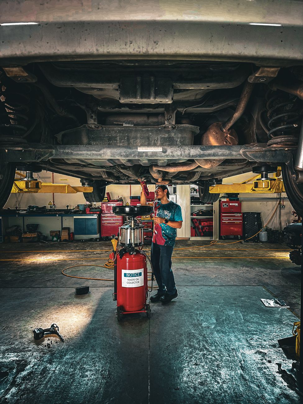 Mechanic checking the underside of a car raised on a lift in a bright workshop bay