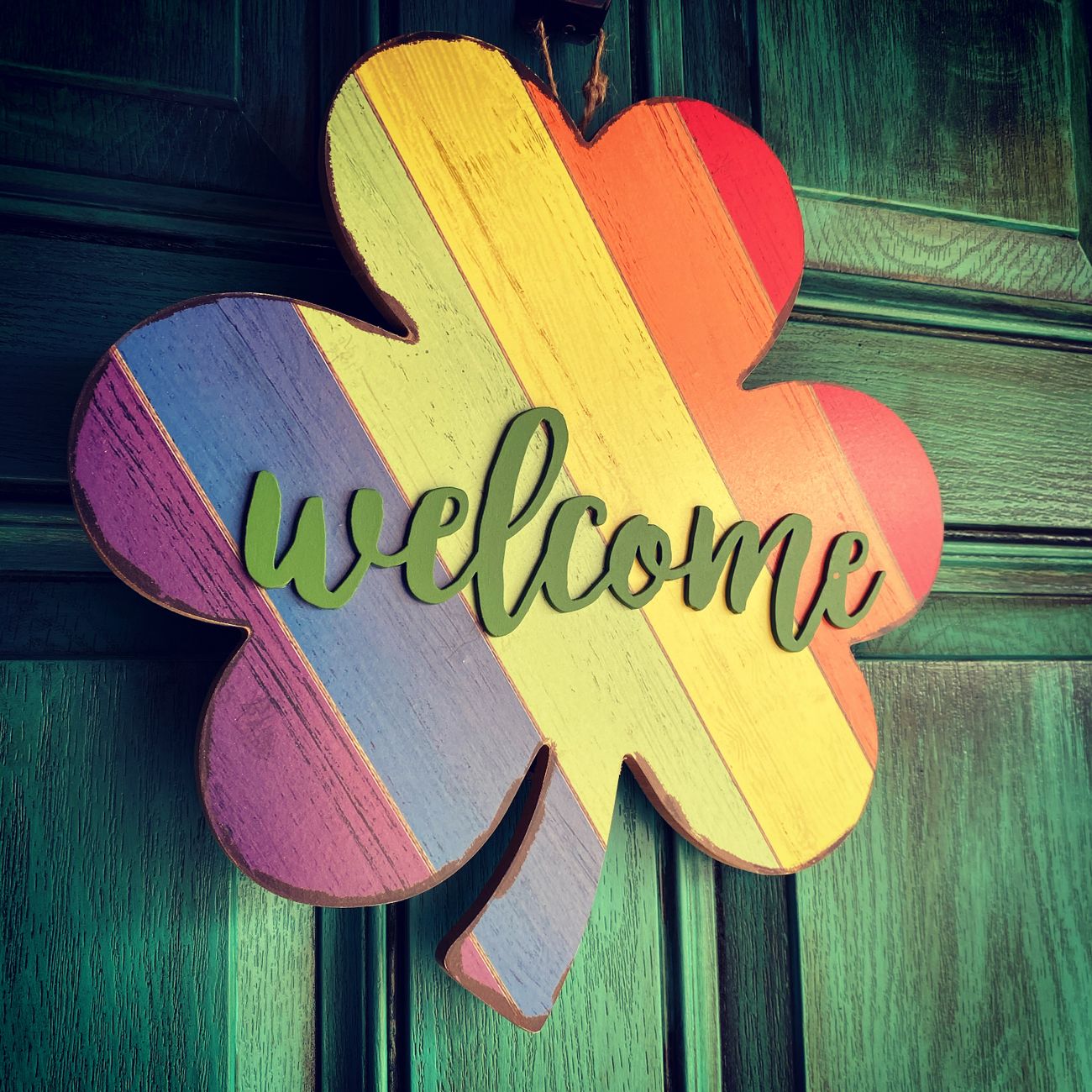 A green door with a rainbow shamrock welcome sign
