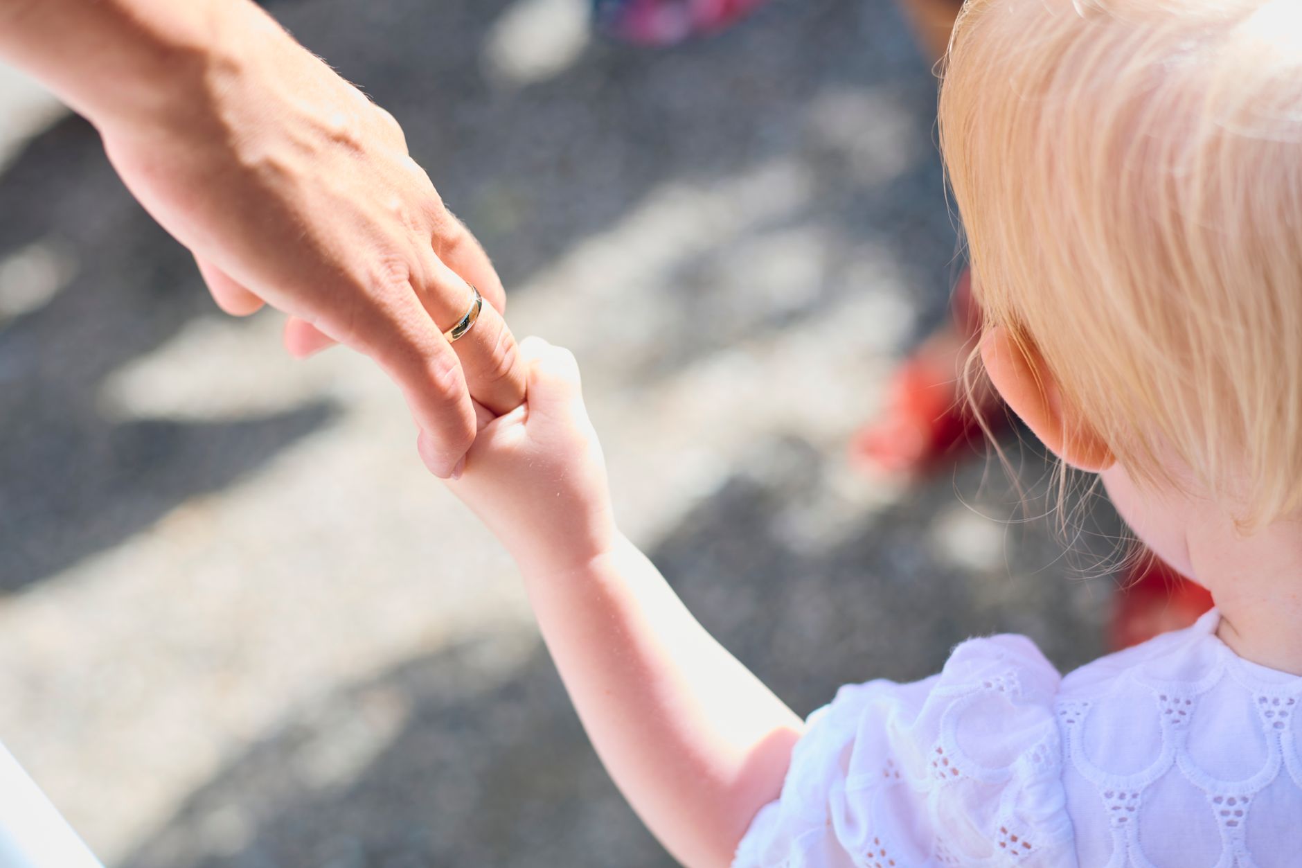 A blonde child holding a parent's hand outdoors