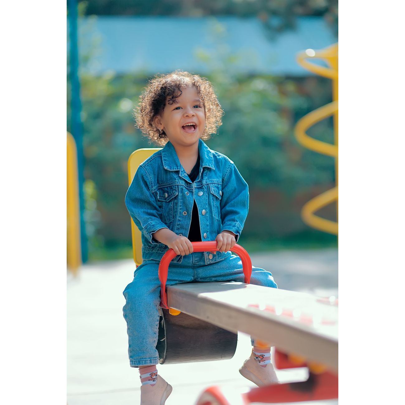 A happy child in a denim jacket on a playground seesaw