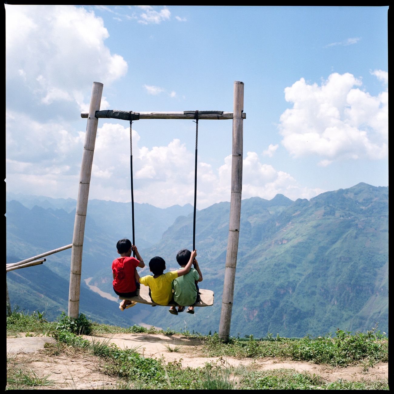 Three children on a swing with mountains behind them