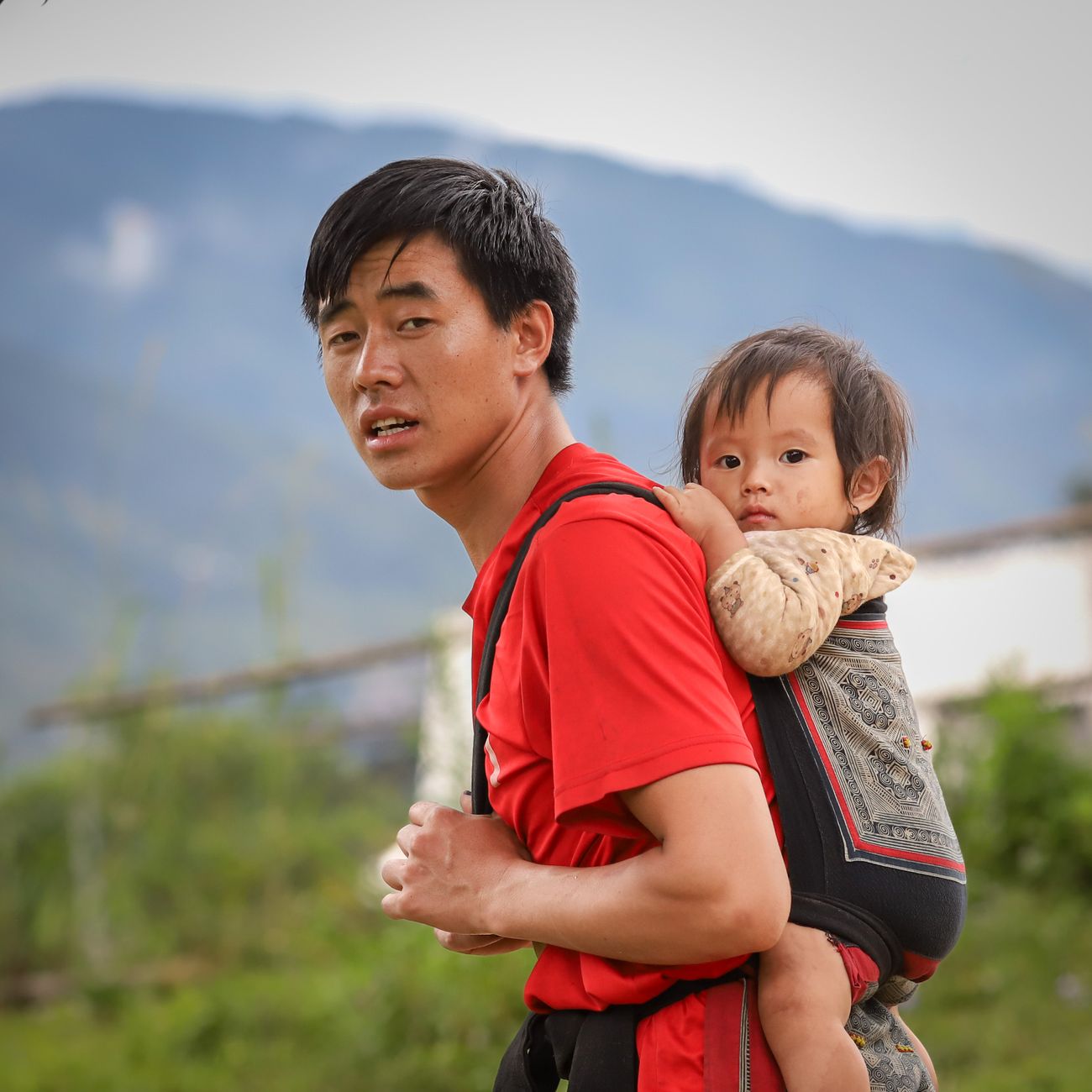 A father carrying his child in a wrap with mountains behind