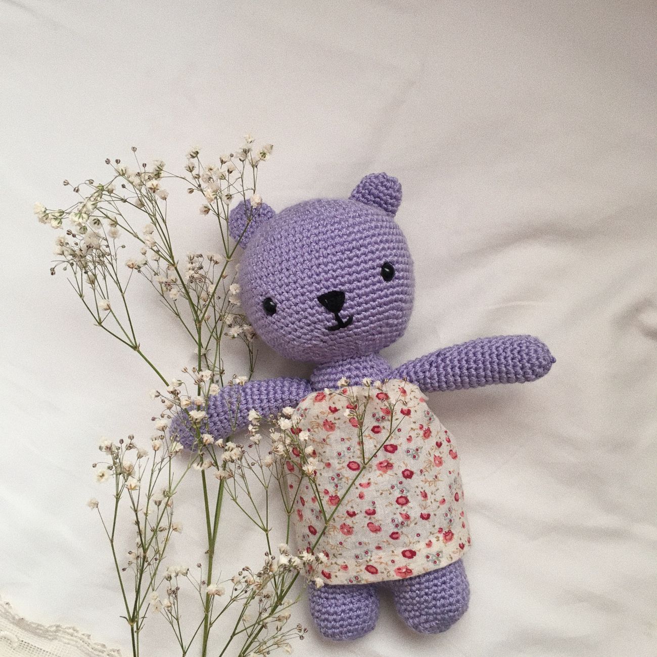 A purple crochet teddy bear resting on a soft white blanket